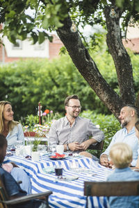 Friends talking while sitting at dining table in garden party during summer weekend