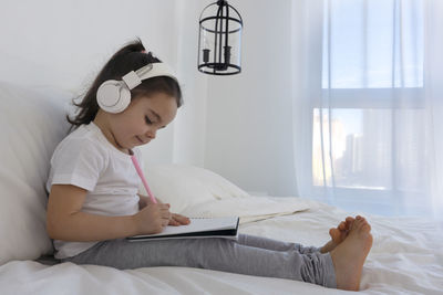 Side view of woman using digital tablet while lying on bed at home