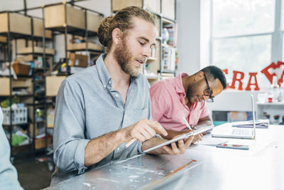 Businessman using tablet computer while male colleague writing on paper at table