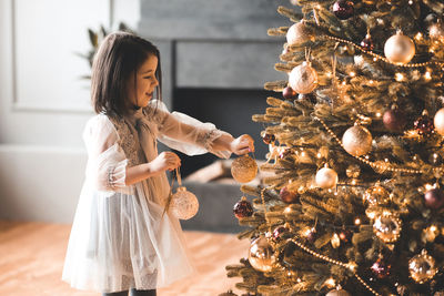 Cute girl decorating illuminated christmas tree at home