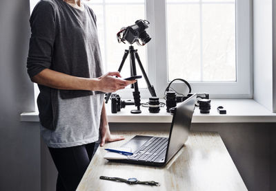 Midsection of woman using smart phone while standing by table