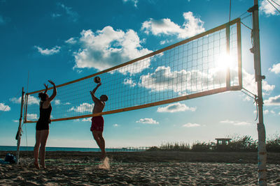 Man and woman playing volleyball against cloudy sky during sunny day