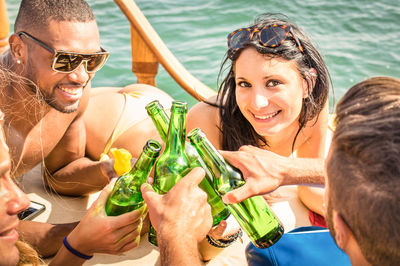 Portrait of young woman smiling while toasting beer bottles on boat in sea