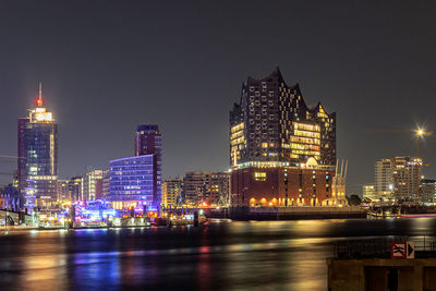 Illuminated buildings by river against sky in city at night