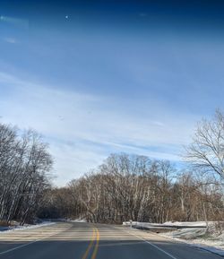 Road by bare trees against sky