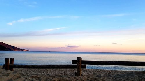 Wooden posts on beach against sky during sunset