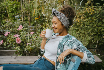 Smiling female farmer drinking coffee while sitting at urban farm