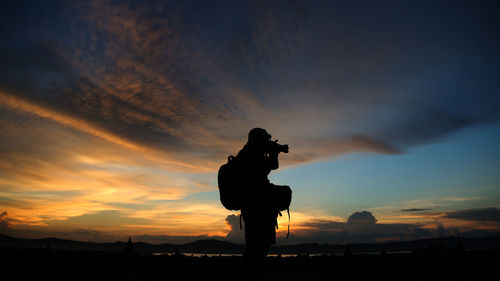 Silhouette woman photographing against sky during sunset