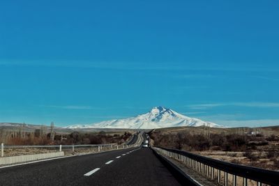 Road leading towards snowcapped mountains against sky