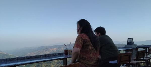 Rear view of woman standing on railing against clear sky