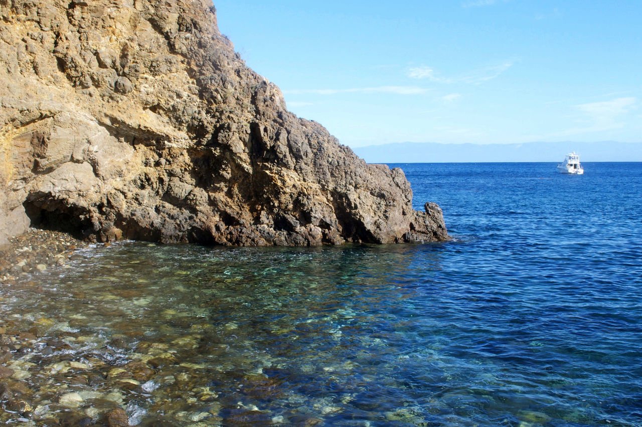 sea, water, scenics, waterfront, tranquil scene, tranquility, beauty in nature, horizon over water, sky, blue, rock formation, nature, rock - object, rippled, cliff, idyllic, rock, seascape, day, nautical vessel