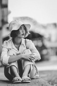 Full length of woman wearing hat sitting on road