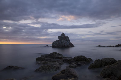 Rocks in sea against sky during sunset