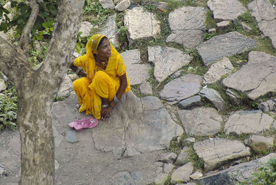 High angle view of smiling woman in yellow sari sitting on rock