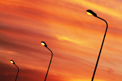 Low angle view of illuminated street lights against cloudy sky during sunset