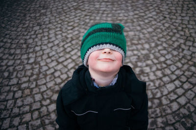 Boy with eyes covered by knit hat on cobblestone street