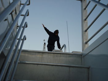 Low angle view of man with hand raised seen through steps against clear sky