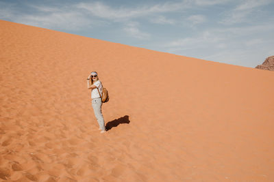 Young woman standing on sand dune in desert against sky
