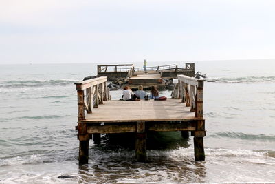 Friends sitting on broken pier over sea