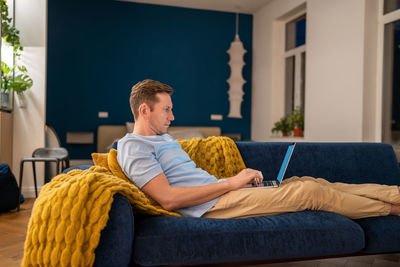Man sit on couch with laptop on lap studying, relaxing, chilling, browsing internet, checking news