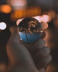 Cropped hand holding crystal ball at night