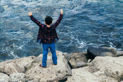 Rear view of boy standing on rock against sea