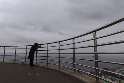Side view of mature woman photographing while standing on observation point against sky