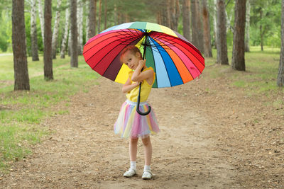 Happy funny girl holding rainbow umbrella. cute happy schoolgirl playing in rainy summer park. 