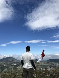 Young man holding flag standing against landscape