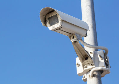 Low angle view of security camera against clear blue sky