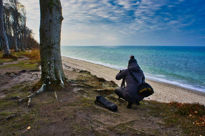 Rear view of woman photographing sea while crouching at beach