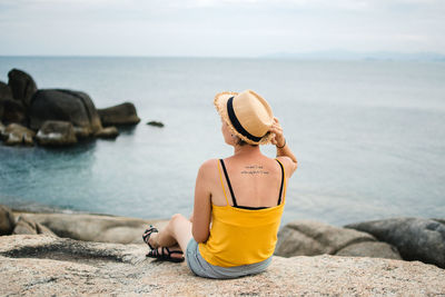 Rear view of man sitting on rock by sea