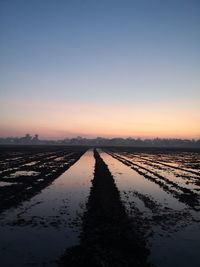 Canal amidst field against sky during sunset