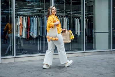 Happy confident smiling plus size curvy young woman with shopping bags walking on city street near