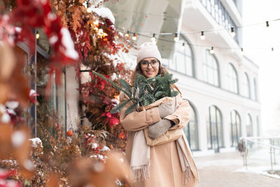 A stylish young woman wearing a hat with branches of nobilis in a bag walks around the christmas 