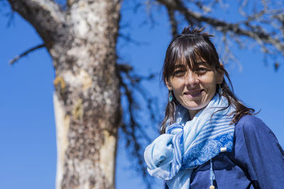 Portrait of smiling woman against tree trunk