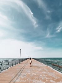 Rear view of woman walking on pier over sea