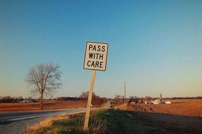 Signboard on road against clear blue sky