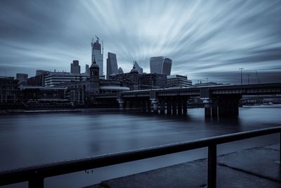 Bridge over river by buildings against sky in city