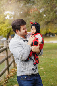 Father carrying baby daughter while standing in park