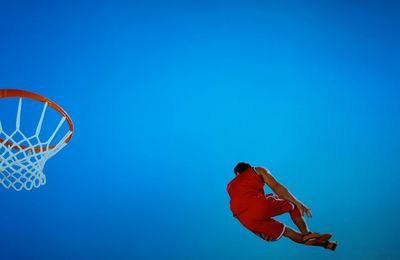 Low angle view of male basketball player jumping against clear blue sky