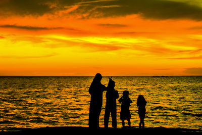 Silhouette people by sea against sky during sunset