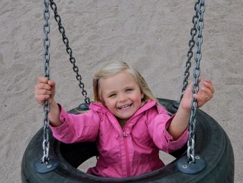 Portrait of smiling girl sitting on swing at playground