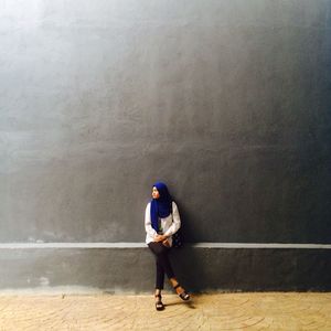 Young woman sitting against gray wall