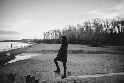 Side view of woman standing on beach against sky