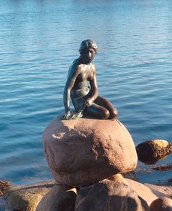 Full length of shirtless man sitting on rock by lake