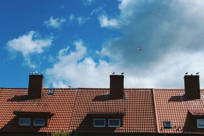Low angle view of seagulls perching on chimneys against cloudy sky