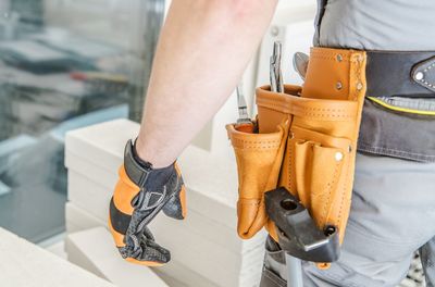 Midsection of worker with work tools standing in workshop