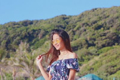 Smiling young woman wearing sunglasses while standing against mountain during sunny day