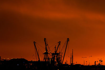 Silhouette cranes at harbor against sky during sunset